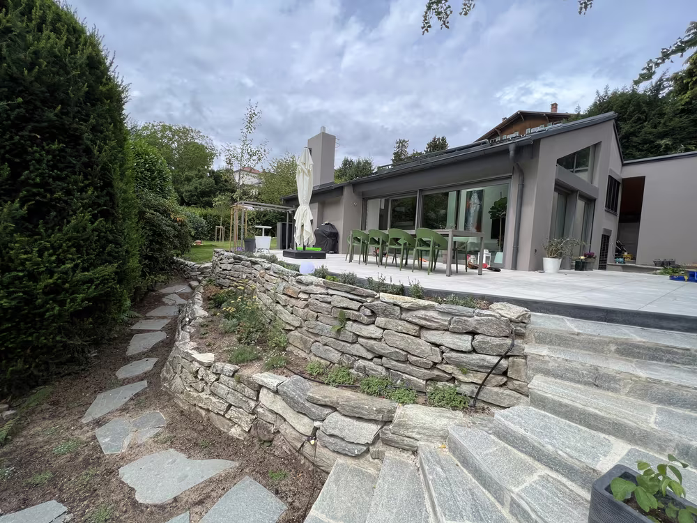 Geschwungene Natursteinmauer mit Steintreppe und Terrasse an einem Neubau in Königstein